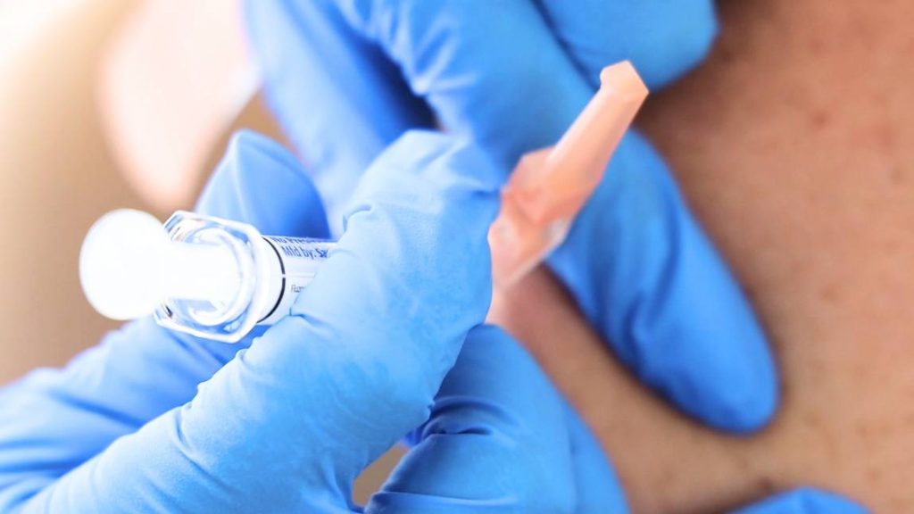 close up of a nurse with blue surgical gloves giving a flu shot in the upper arm of a patient