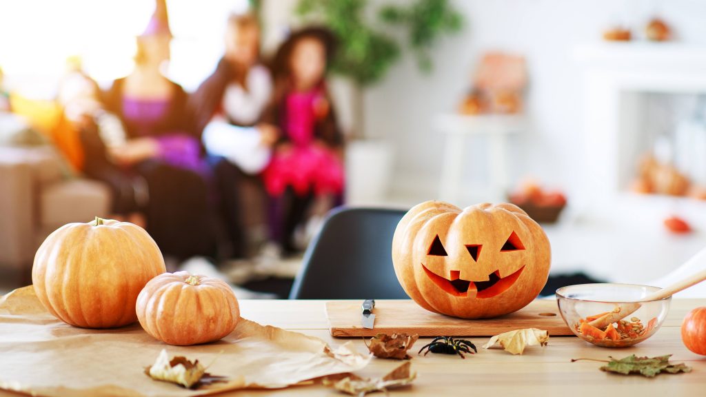 a table with Halloween pumklins and leaves, with children (out of focus) in the backgound in costumes