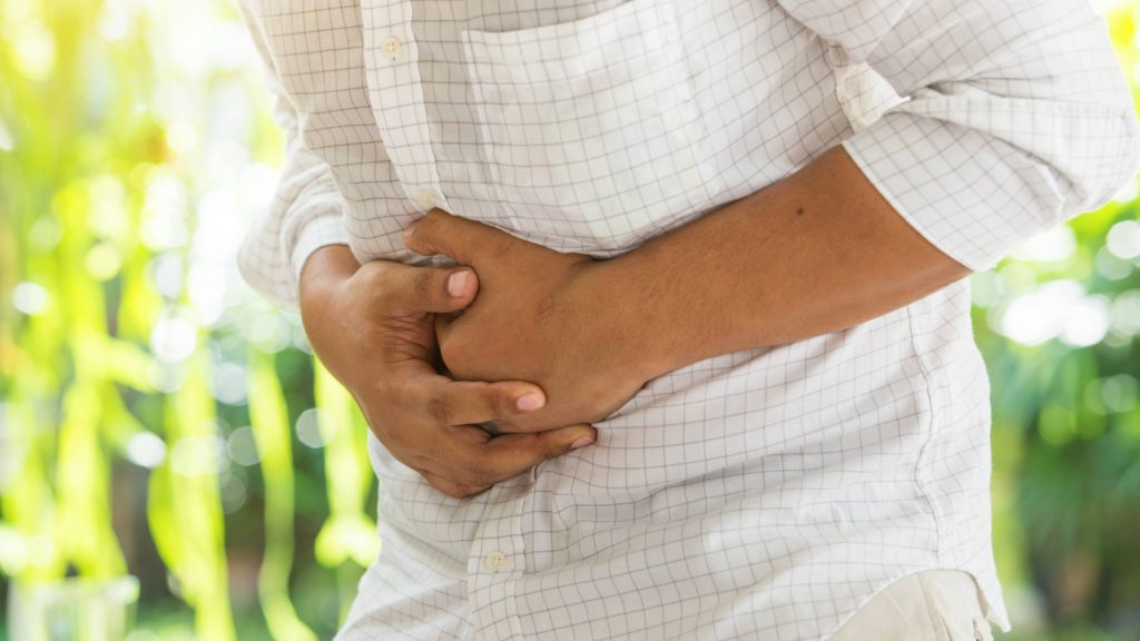 a young man, perhaps Latino, crossed his arms around his stomach in pain