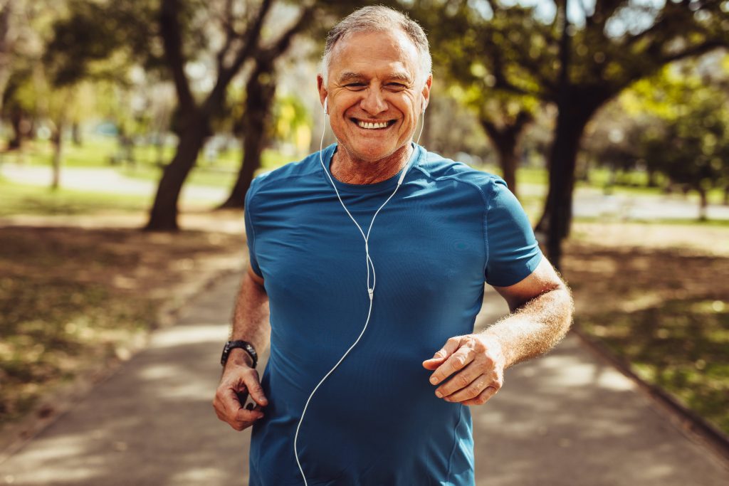 a smiling older man out for a run on a sunny day, wearing earbuds