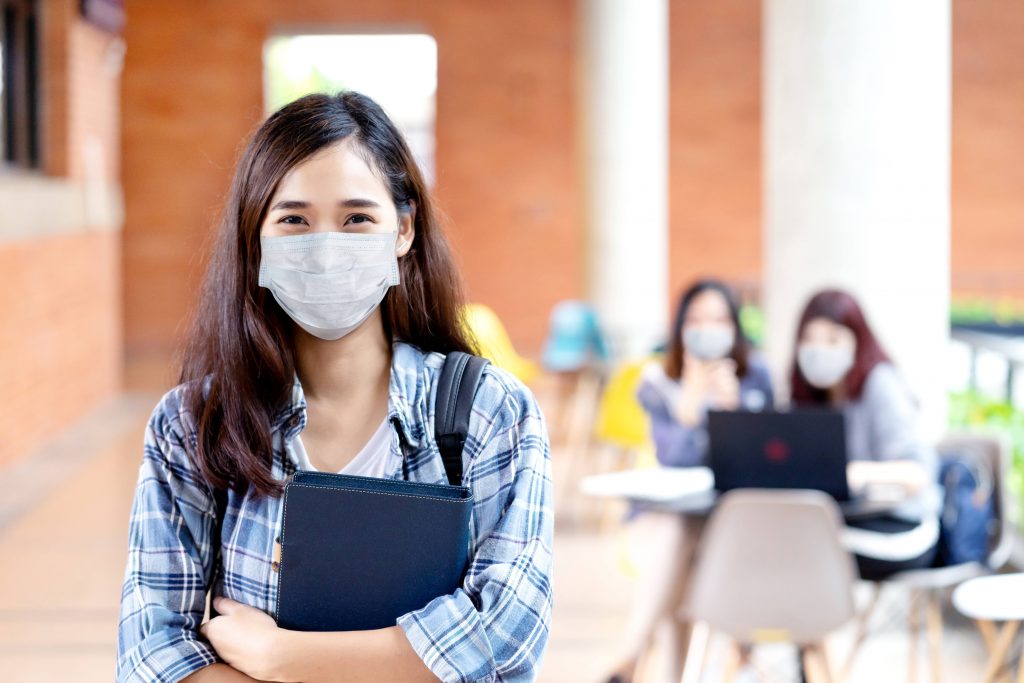 a young white, perhaps Asian, teenage girl wearing a face mask and holding a high school or college planner book