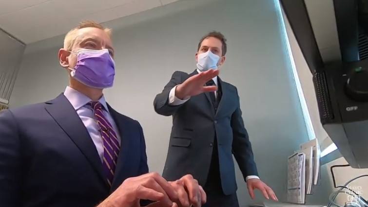 Dr. Laskowki wearing a facemask and sitting at a computer with a colleague, also wearing a facemask, demonstrating ergonomic recommendations