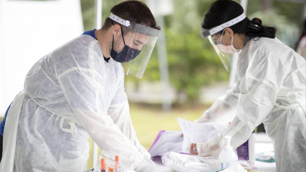 Mayo Clinic medical personnel in Florida, a white man and a white woman wearing PPE, preparing an outside table for drive-through COVID-19 testing
