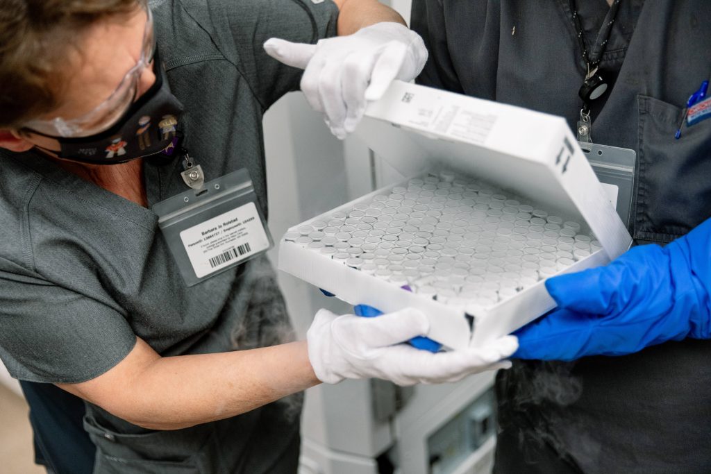 Mayo Clinic medical staff in Rochester, wearing PPE, inspecting a box of Pfizer vaccine vials after arrival
