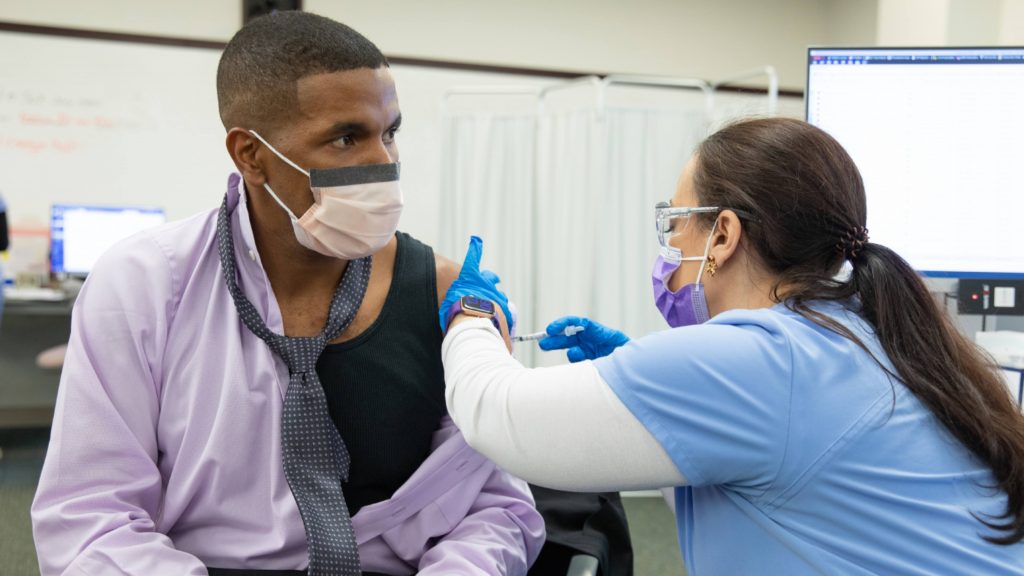 a Mayo Clinic employee in Florida, a Black man, wearing a mask and receiving the COVID-19 vaccine