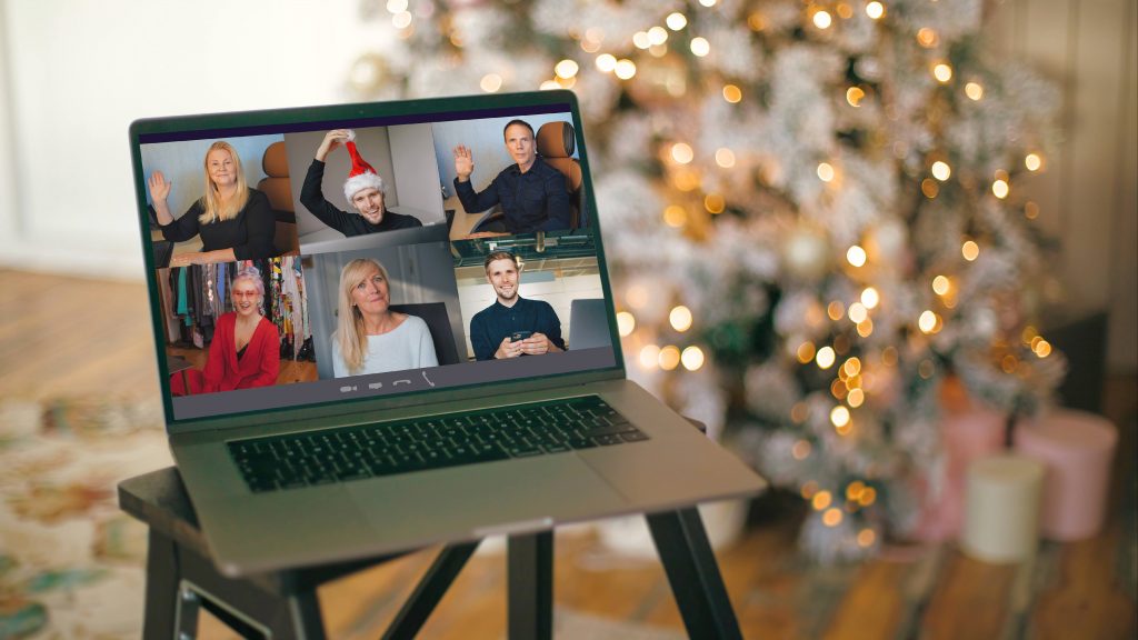 a computer laptop with a number of people in a virtual meeting, perhaps on Zoom, on a stool in front of a a decorated Christmas tree