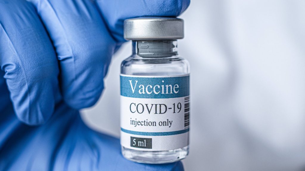 close up of COVID-19 vaccine vial being held by a person wearing a blue PPE glove