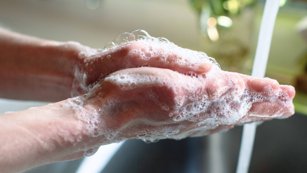 close up of a white person washing their hands under running water from a tap in a sink and using soap, washing hands helps reduce risk of respiratory infections