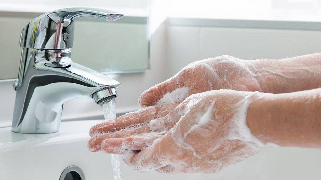 close up of a white person washing their hands under running water from a tap in a sink and using soap