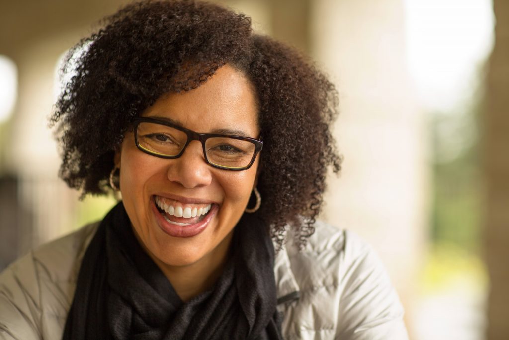 a middle aged Black woman with short hair, glasses and earrings on, laughing and smiling, looking happy