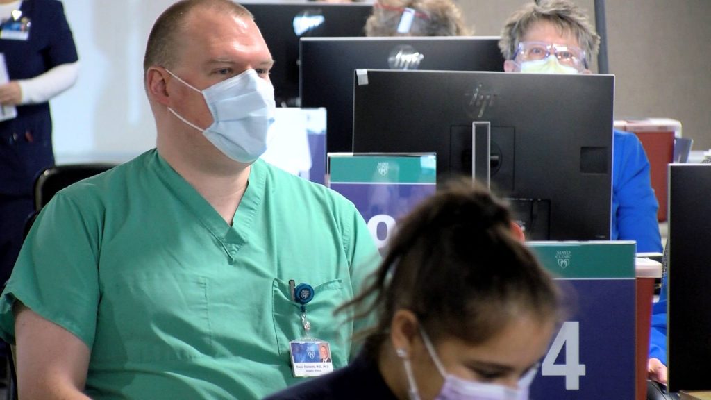 Mayo Clinic's Dr. Casey Clements, a white man, wearing scrubs and a mask while waiting to receive his COVID-19 vaccine