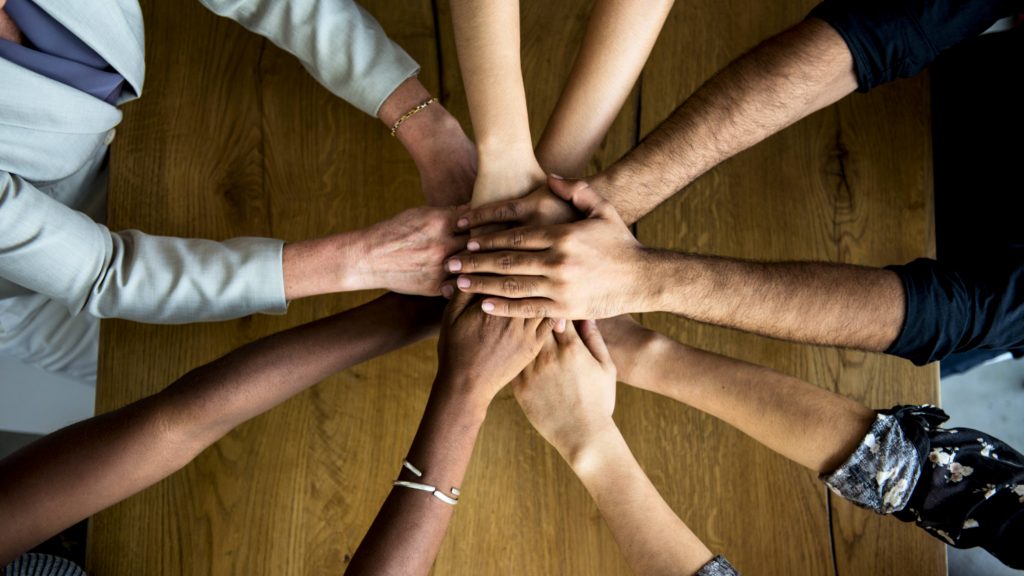 a circle of people's hands and arms coming together as a diverse community like a work team