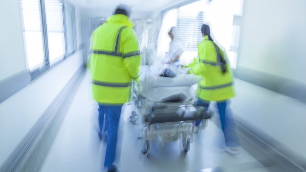 a slightly out of focus image of a hospital hallway with emergency staff walking quickly pushing a gurney with an injured patient