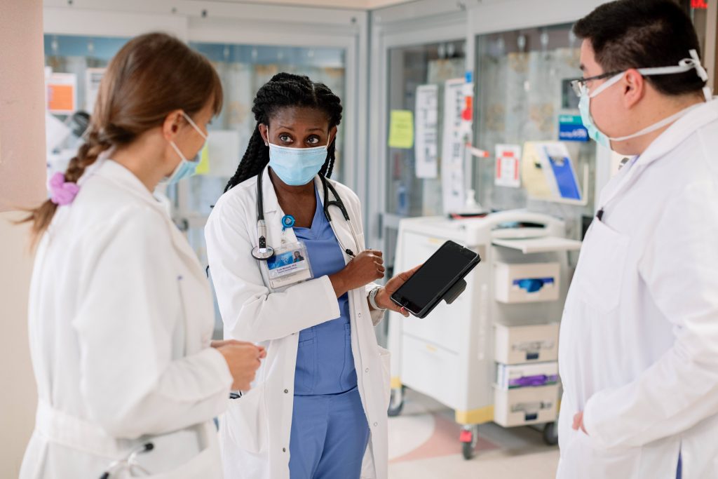 three Mayo Clinic medical staff people, a white woman, a Black woman, and a white man, in scrub uniforms with white lab coats and wearing face masks in the hospital