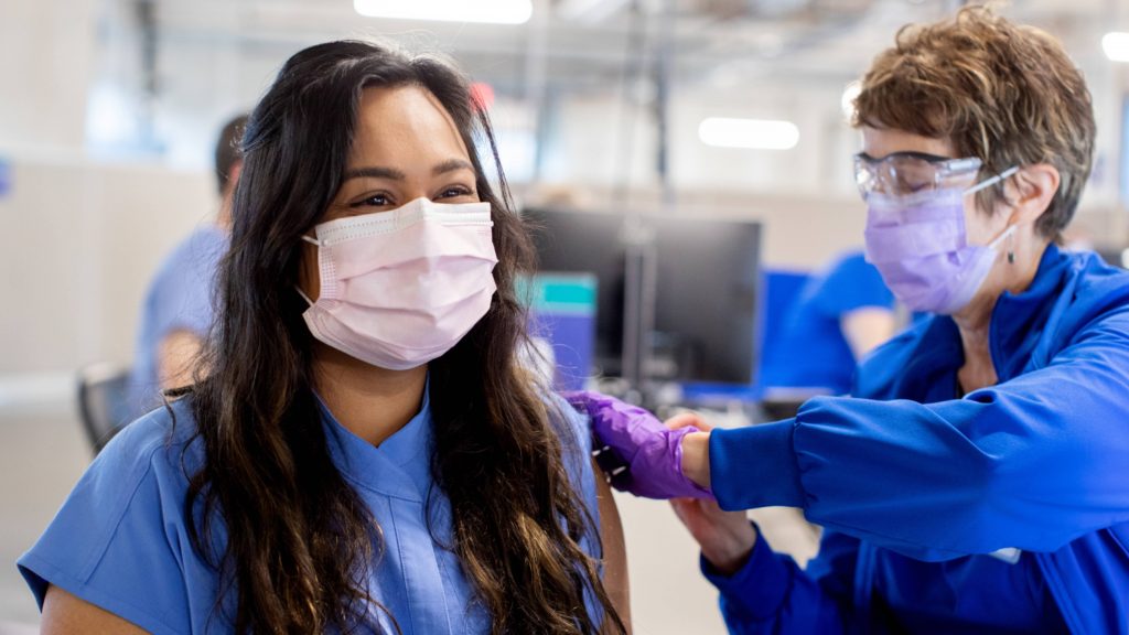 a Mayo Clinic employee, a woman with dark hair and wearing a mask, receiving a COVID-19 vaccine
