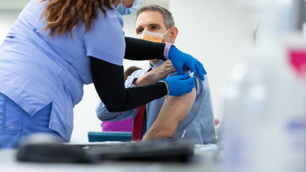 Profesional de la salud preparando la parte superior del brazo de un hombre para la vacunación contra COVID-19