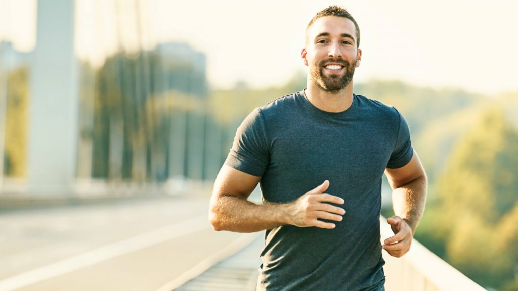 a young white man smiling while running, jogging, exercising outside