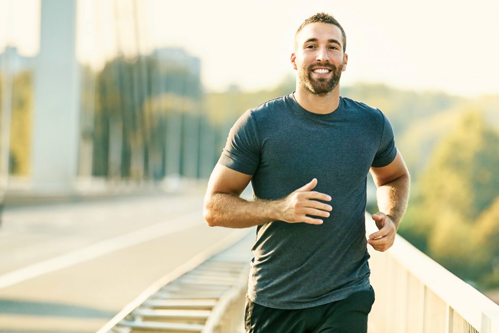 a young white man smiling while running, jogging, exercising outside