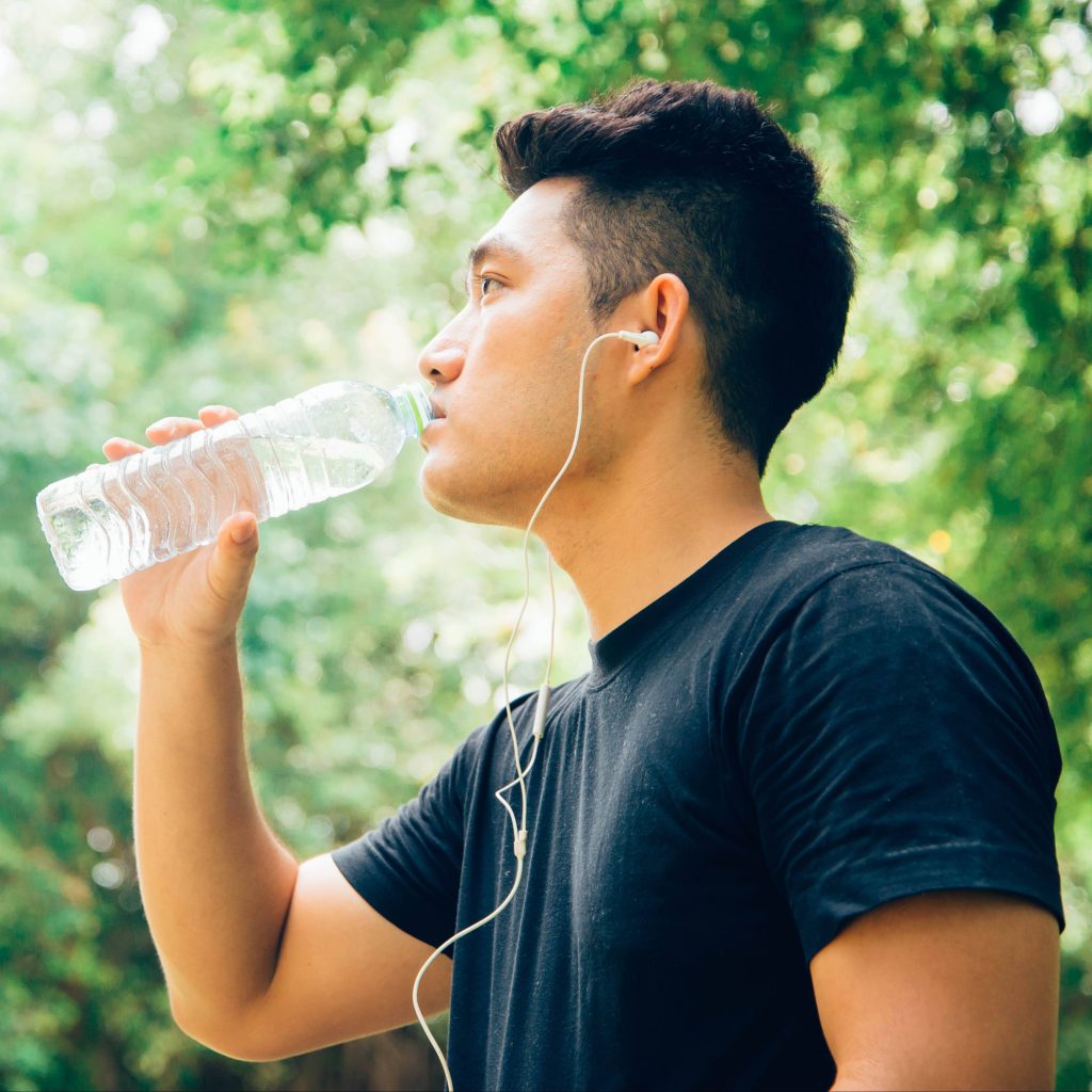 a young Asian American man outside exercising, wearing ear buds for music and drinking a bottle of water