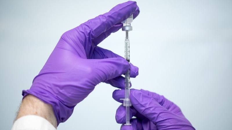 purple gloved hands filling syringe from a vaccine vial