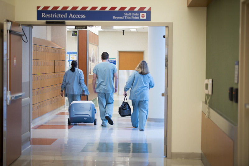 3 medical staff in scrubs walking in a hallway with one pulling a cooler used for organ transport