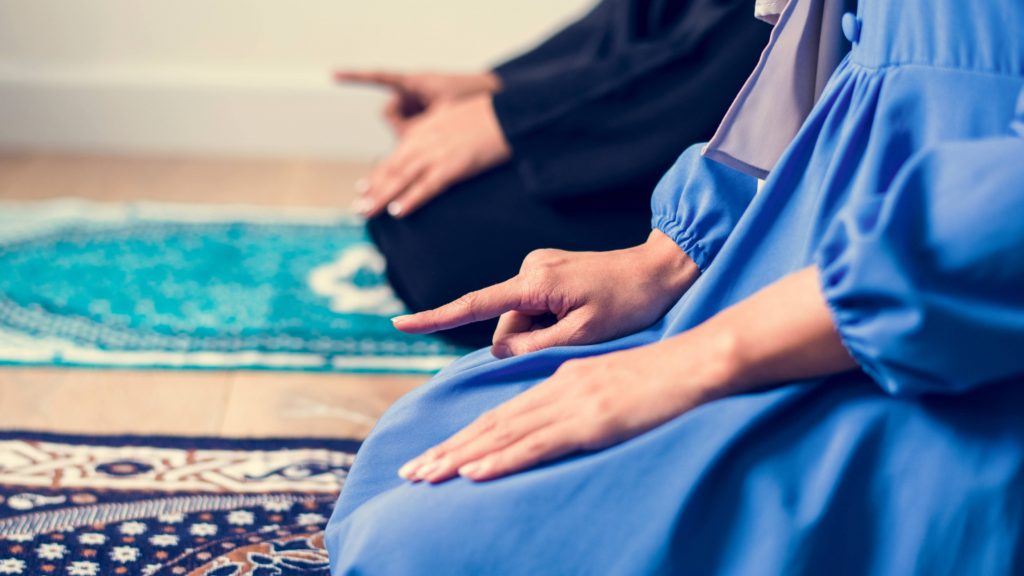 two people kneeling on a prayer rug and praying, perhaps during the Islamic Ramadan