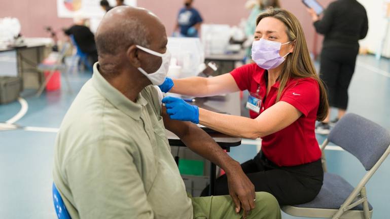a Mayo medical staff person, white woman, administering a COVID-19 vaccine to an adult Black man, both wearing masks