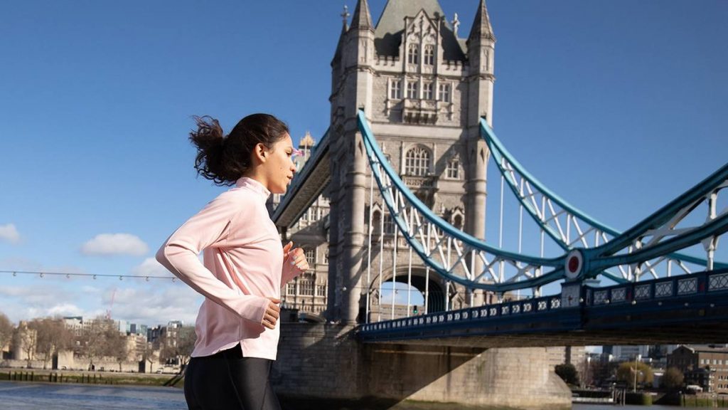 Una mujer joven en ropa deportiva corriendo a lo largo del río Támesis y el puente en Londres