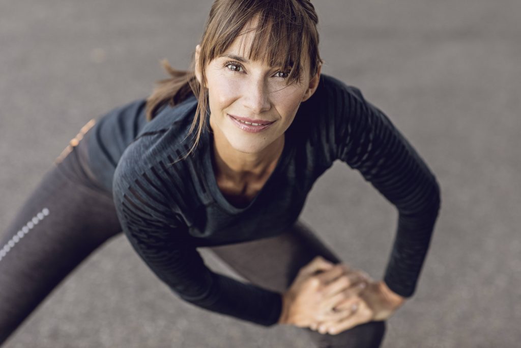 a middle aged white woman smiling and doing warmup exercise and stretching