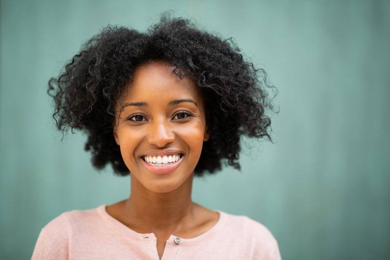 a young Black woman in a light summer shirt with a green background smiling and happy