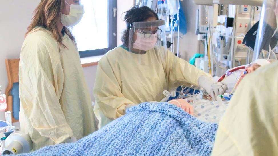 Mayo Clinic medical personnel in full PPE tending to a patient with COVID-19 in a hospital bed