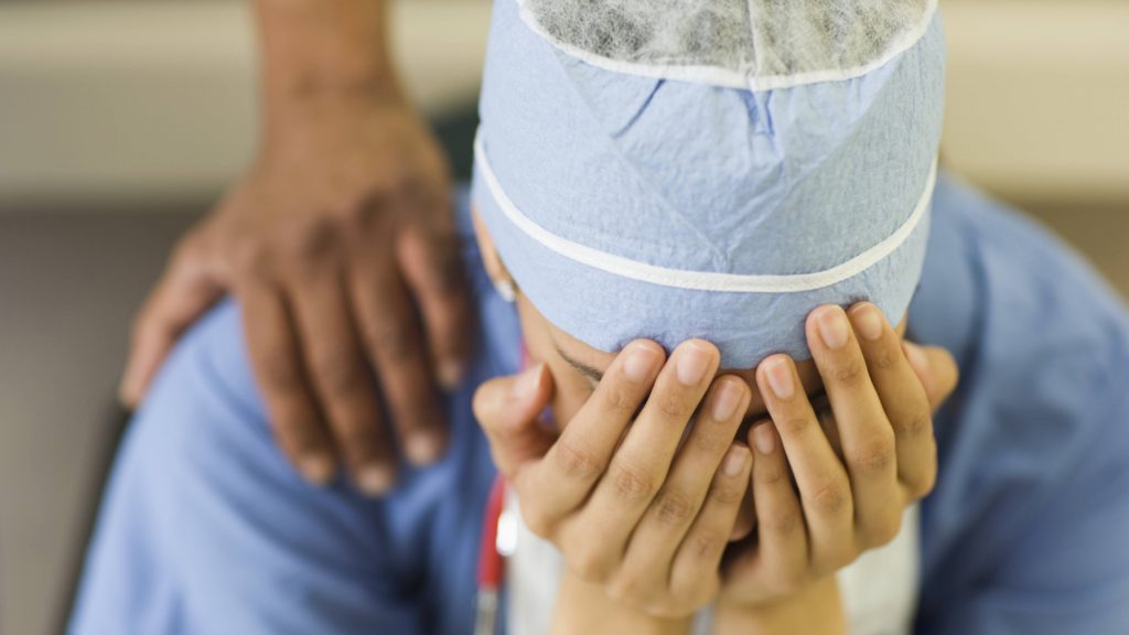 a person, a nurse or doctor, in medical scrubs holding their head in their hands in exhaustion, sadness, burnout