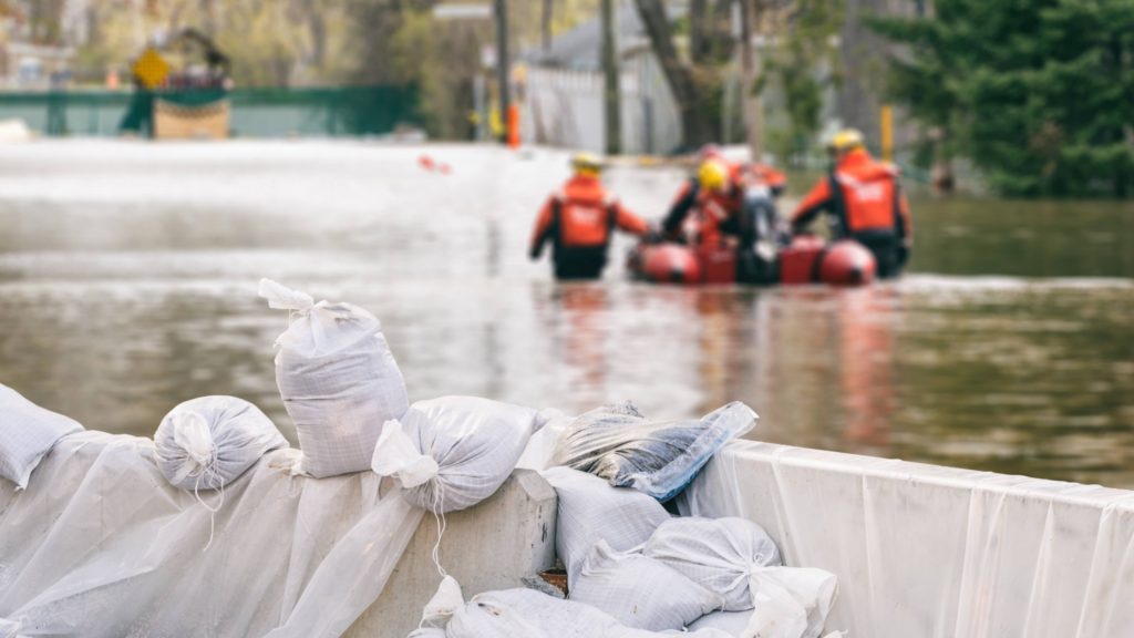 a storm flooded stream or street with sandbags and emergency teams with a rescue raft