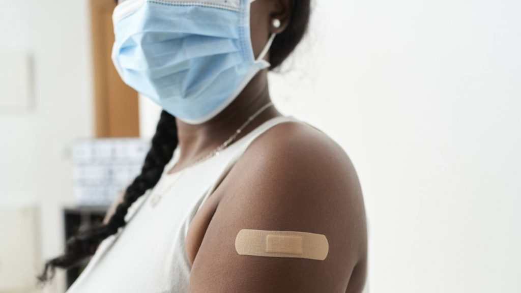 a young Black woman wearing a mask and with a bandaid on her arm after having a vaccination shot