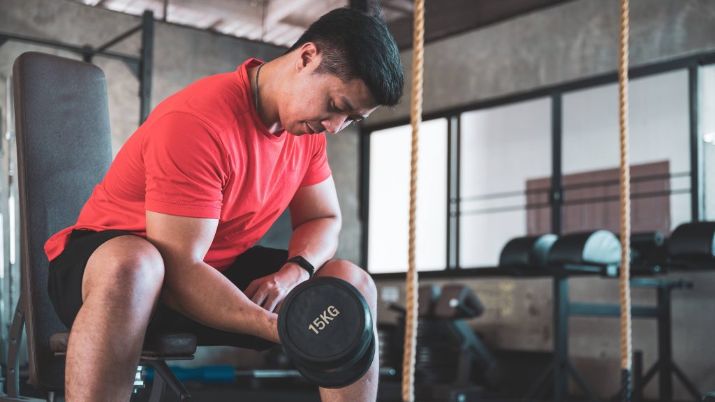 a young or middle aged Asian man in a workout gym lifting weights and exercising