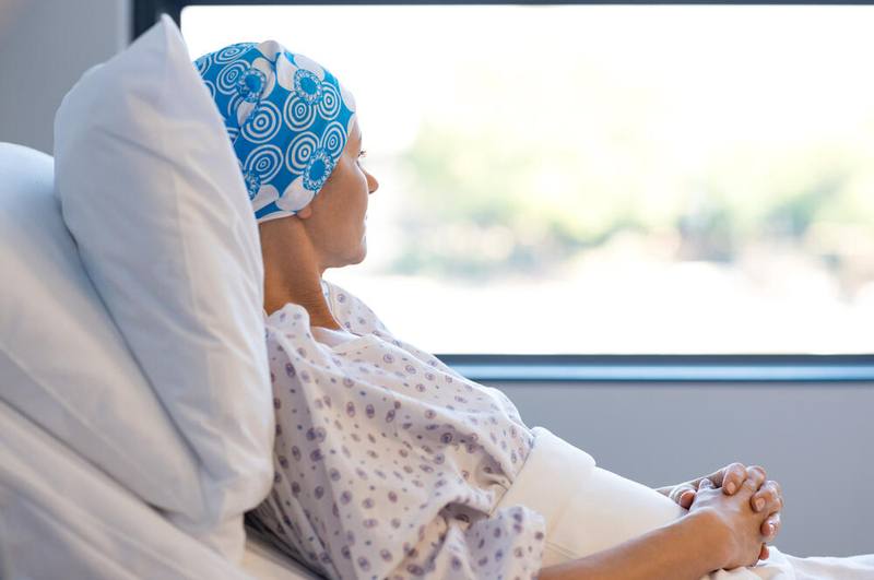 a young white woman in a hospital bed, looking out a window, wearing a headscarf because of chemo treatment for cancer