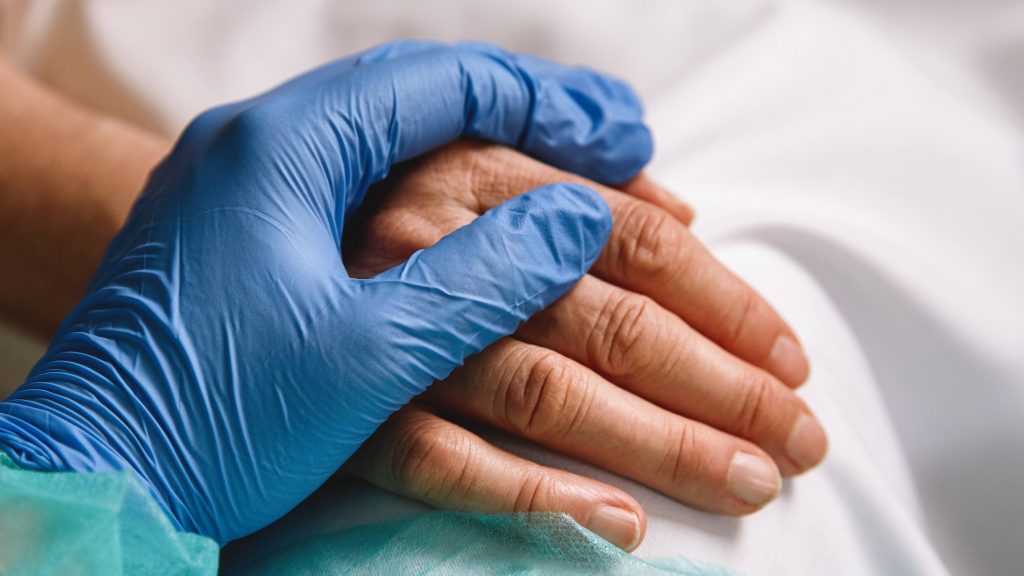 closeup of a health care provider's hand with a medical glove holding a patient's hand in a hospital bed