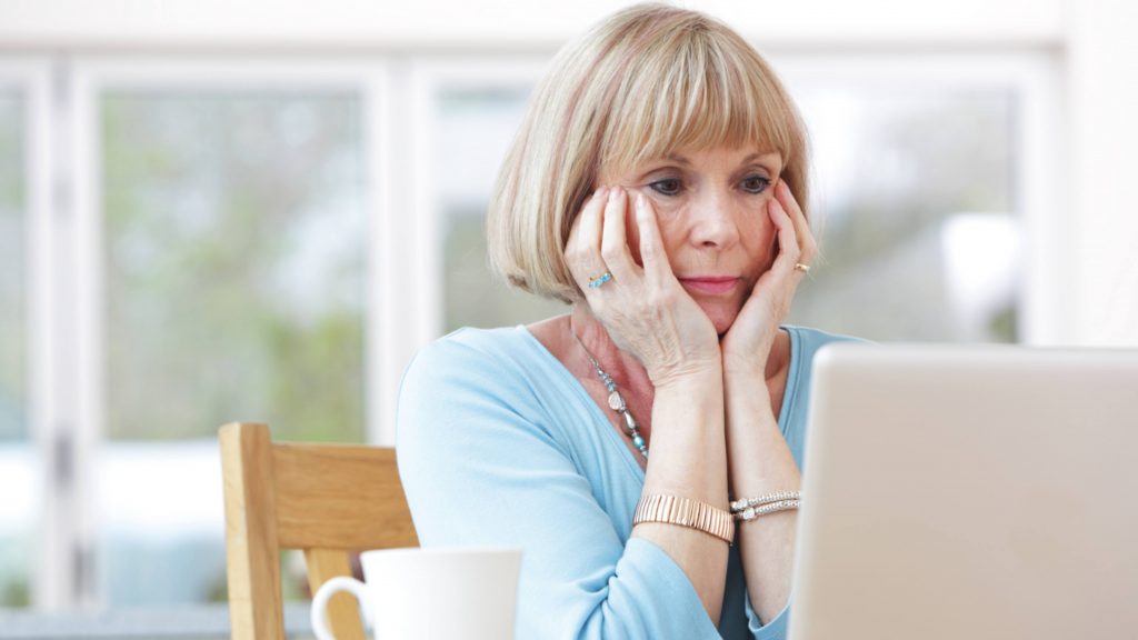 a middle-aged white woman worried, concerned with her head in her hands looking at a computer laptop