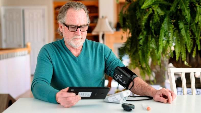 a white middle aged man wearing glasses and taking his blood pressure for home telehealth monitoring