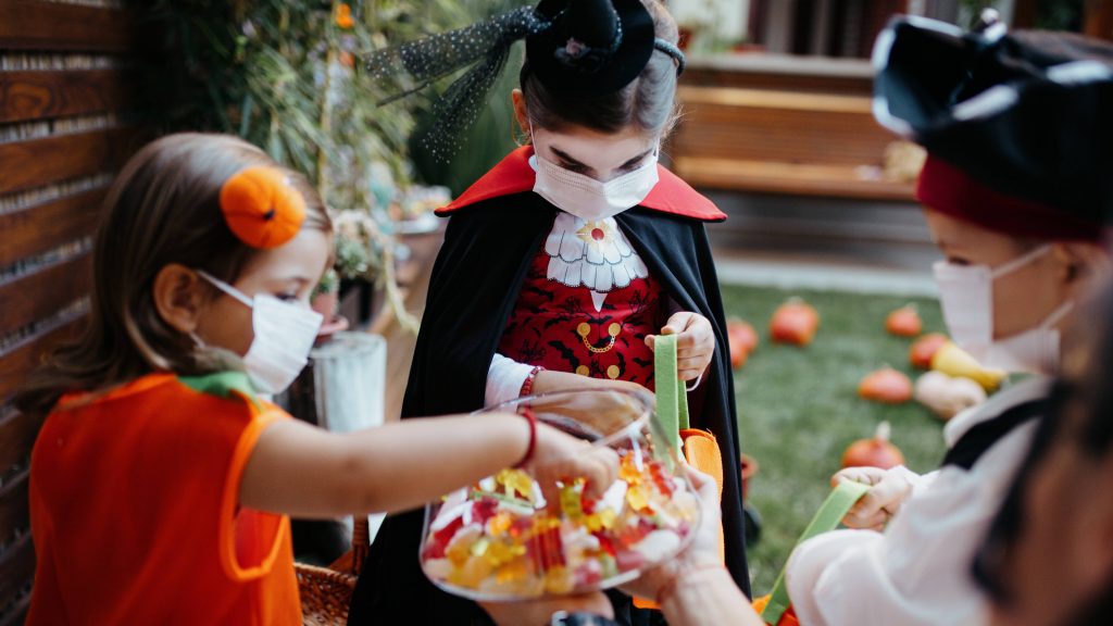 a group of young children in Halloween costumes, trick or treating, wearing face masks, COVID-19