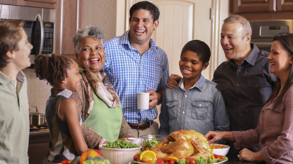 a happy group of family and friends gathering in a kitchen around a turkey dinner for holiday meal