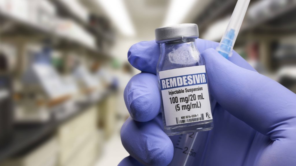 a person wearing blue medical gloves holding a vial of the COVID-19 therapy medication remdesivir