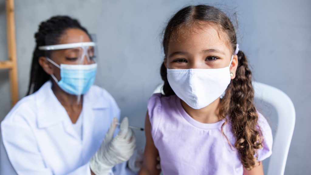 an elementary school aged Latina or Black girl wearing a mask getting a vaccination