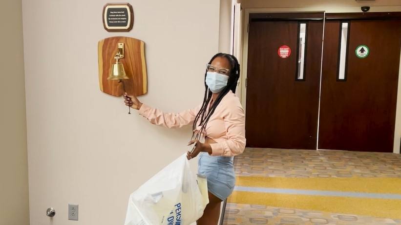 young Black woman, breast cancer patient Jessica Florence, wearing mask and ringing the bell
