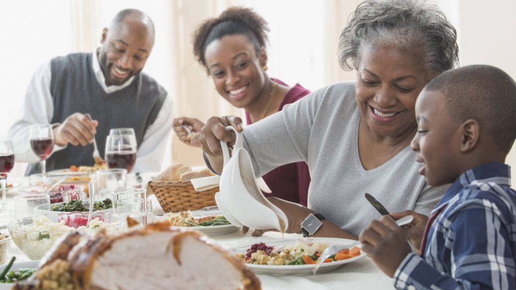 a Black family of several generations having fun at Thanksgiving dinner table
