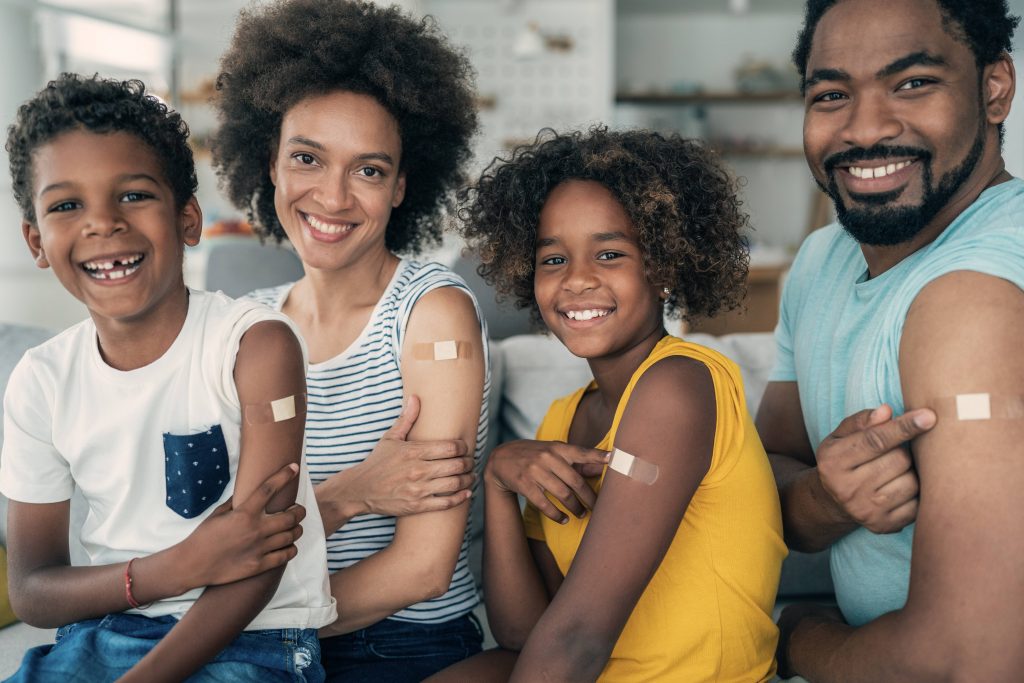 a Black family with two children all with vaccination bandaids on their arms