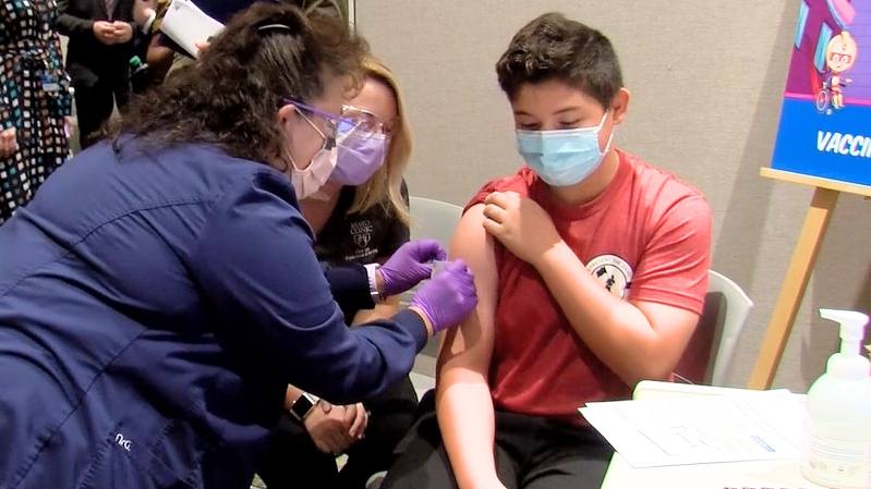 a young boy wearing a mask receiving a COVID-19 vaccine