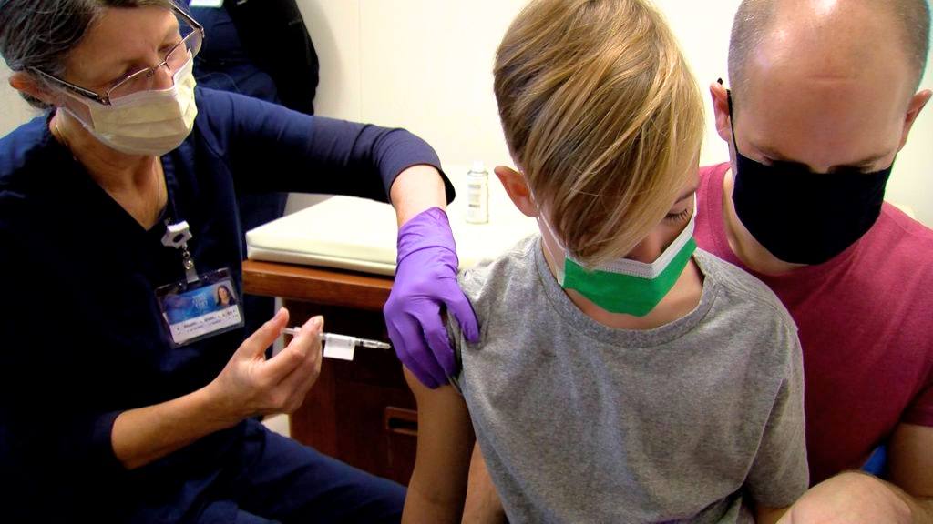 an elementary school aged white boy with mask receiving COVID-19 vaccine
