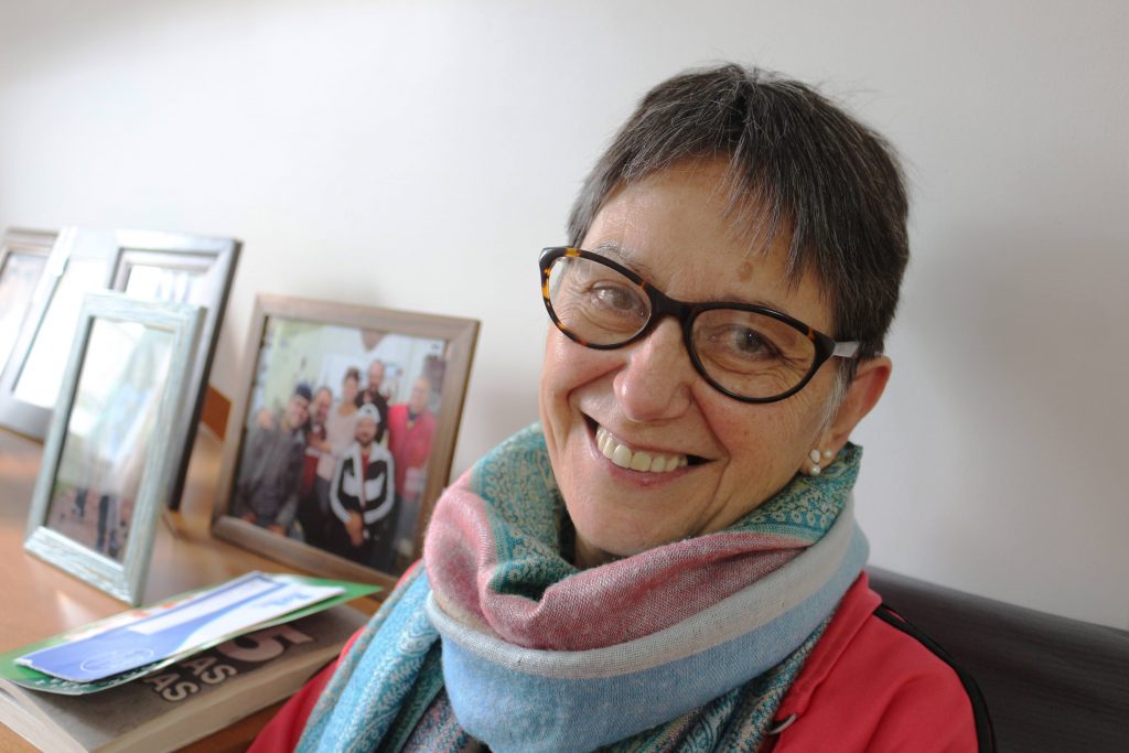 happy middle aged white woman wearing glasses and smiling with framed family photos in background