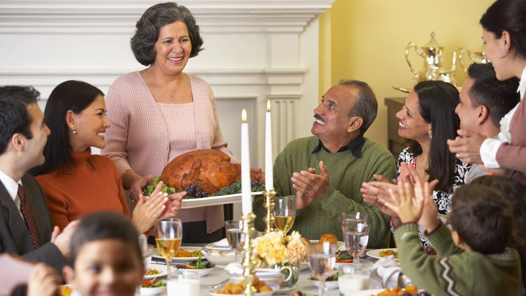 multi-generational family, perhaps Latino or West Asian, celebrating Thanksgiving holiday with turkey and festive table